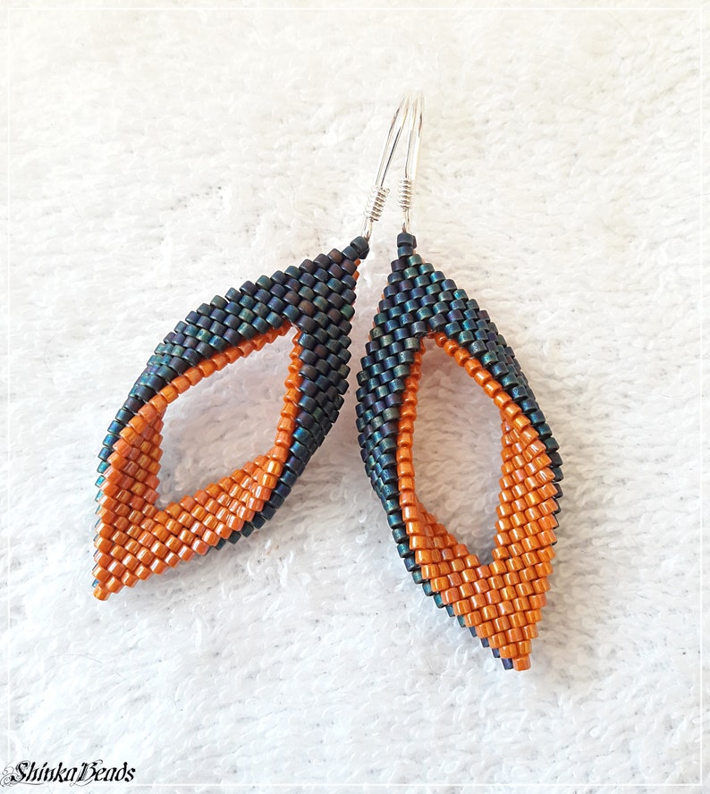 May include: A pair of dangle earrings with a twisted design. The earrings are made with orange and dark green beads.