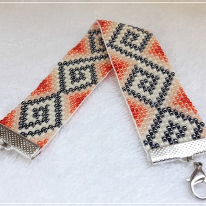 May include: A beaded bracelet with a geometric pattern in shades of orange, white, and black. The bracelet has a silver clasp.