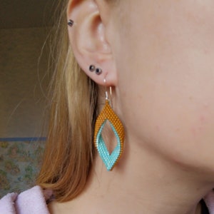 May include: A pair of dangle earrings with a teardrop shape. The earrings are made of blue and orange beads and have a silver hook.