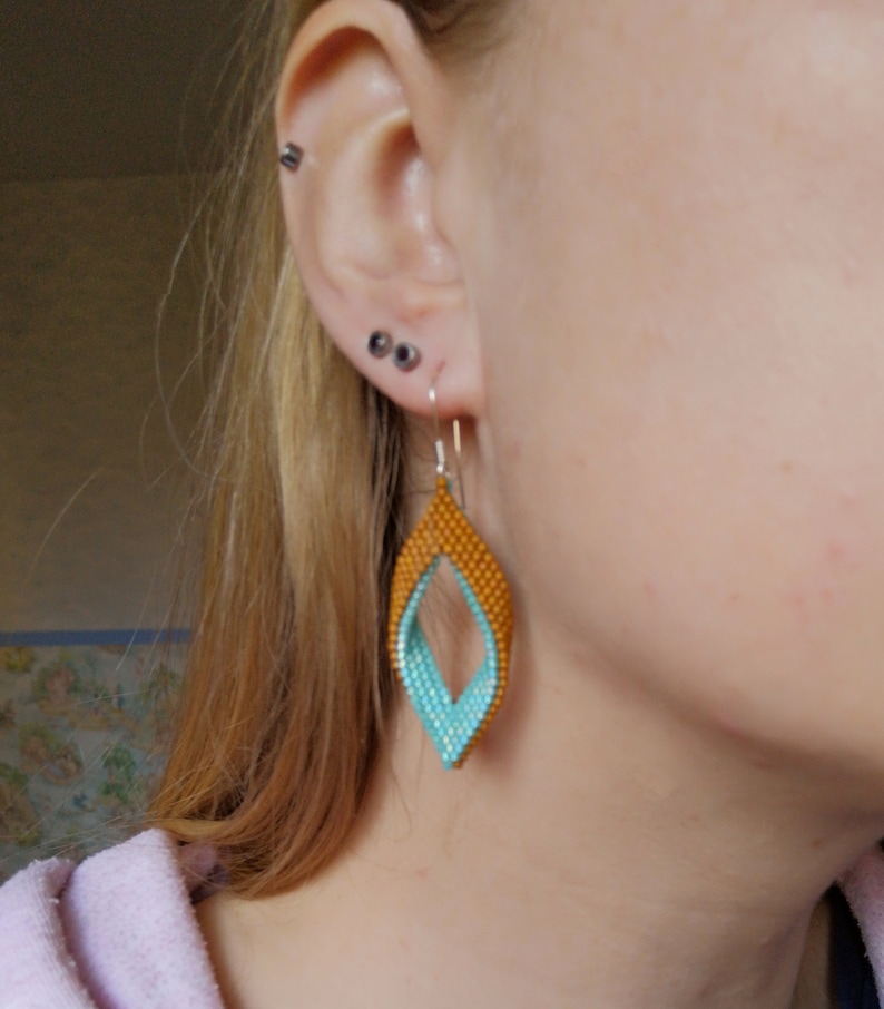 May include: A pair of dangle earrings with a teardrop shape. The earrings are made of blue and orange beads and have a silver hook.