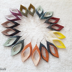 May include: A collection of 12 pairs of beaded earrings in various colors, including black, white, red, orange, yellow, green, and brown. The earrings are arranged in a circle on a white surface. Each earring is made of two overlapping teardrop shapes, creating a unique and stylish design.