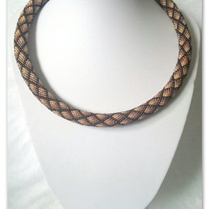 Pode incluir: Um colar de contas castanho e bege com um padrão de diamante. O colar é apresentado num busto de manequim branco.