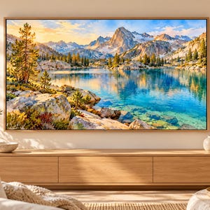 May include: A rectangular framed wall art print featuring a vibrant landscape painting of a clear blue mountain lake surrounded by pine trees and rocky terrain under a golden sunrise sky, mounted on a light-colored wall above a wooden console.