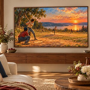 May include: A large rectangular television mounted on a wall displays a vibrant landscape painting of children playing baseball in a field at sunset. The screen shows a warm orange and blue sky over a body of water with trees and figures in the foreground.
