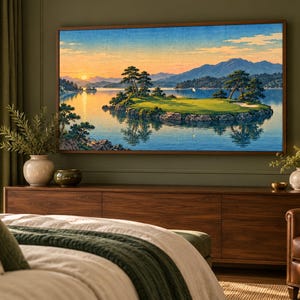 Puede incluir: Una impresi&oacute;n de arte mural rectangular que presenta un paisaje de un campo de golf en una isla rodeada de agua, con pinos, monta&ntilde;as distantes y un cielo al atardecer en tonos naranja, azul y amarillo, enmarcada en un borde de madera marr&oacute;n.