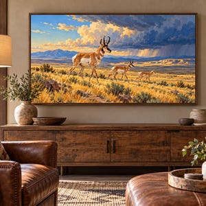 Puede incluir: Una impresi&oacute;n de arte mural rectangular que presenta un paisaje con tres ant&iacute;lopes americanos caminando por un campo de hierba dorada bajo un cielo dram&aacute;tico con nubes de tormenta y monta&ntilde;as lejanas, enmarcado en un borde de madera oscura.