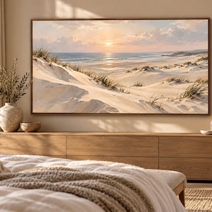 May include: A rectangular landscape wall art print featuring a coastal scene with white sand dunes, beach grass, and a calm ocean under a soft sunset sky. The artwork is framed in a thin wood border and displayed above a long wooden media console.