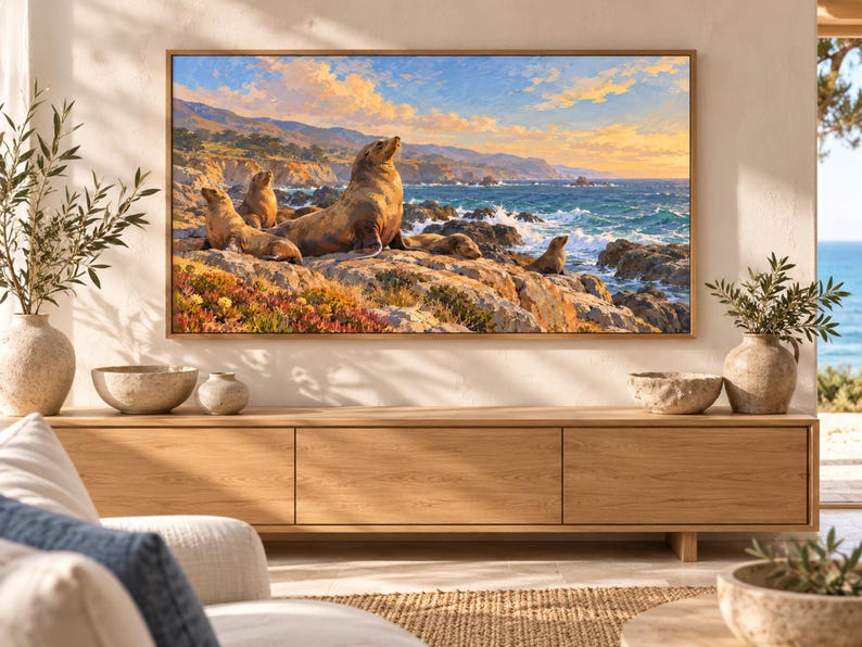 May include: A rectangular wall art print featuring a coastal landscape with several sea lions resting on rocky terrain. The scene depicts a blue ocean with crashing waves under a golden sunset sky, framed in a light-colored wooden border.