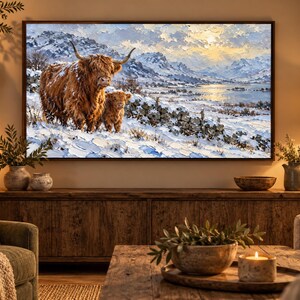 Puede incluir: Una impresi&oacute;n de arte mural rectangular que presenta una pintura al &oacute;leo de una gran vaca Highland marr&oacute;n y un ternero en un paisaje nevado con monta&ntilde;as, un lago y un cielo brillante, enmarcada con un borde fino de madera oscura.