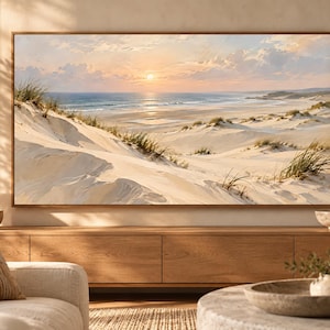 May include: A rectangular landscape wall art print featuring a coastal scene with rolling sand dunes, patches of green beach grass, and a calm ocean under a soft sunset sky with light clouds, all enclosed within a thin, natural wood-toned frame.