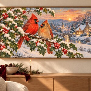 Pu&ograve; includere: Una stampa artistica rettangolare da parete raffigurante due cardinali appollaiati su un ramo di agrifoglio innevato con bacche rosse. Lo sfondo mostra un paesaggio invernale con un cottage in pietra, un ponte e un tramonto sulle colline.