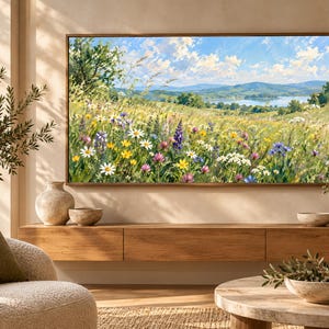 May include: A rectangular landscape painting featuring a vibrant meadow filled with white, yellow, purple, and blue wildflowers under a bright blue sky with fluffy white clouds, displayed in a thin brown frame on a light-colored wall.