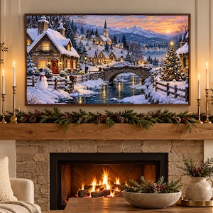 May include: A rectangular wall art print depicting a snowy winter village scene with stone cottages, a stone bridge over a river, a snowman, and a lit Christmas tree under a sunset sky, mounted above a fireplace with a wooden mantel and greenery.