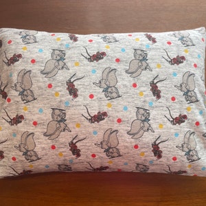 May include: A gray pillowcase with a repeating pattern of cartoon elephants with red, yellow, and blue accents. The elephants are flying through the air with a red and yellow striped object.