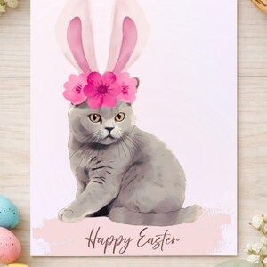 Może przedstawiać: Cyfrowa kartka wielkanocna z szarym kotem w różowych uszach królika i wiankiem z kwiatów. Słowa "Happy Easter" są napisane kursywą pod kotem. Karta ma różowo-białą kolorystykę.