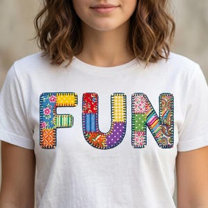 May include: White t-shirt with the word "FUN" in colorful patchwork letters. The letters are made of various patterned fabrics, including floral, striped, and polka dot designs. The shirt is a casual, everyday wear item.
