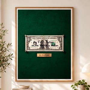 Puede incluir: Una pieza de arte mural enmarcada que presenta un billete de un dólar estadounidense montado sobre un fondo verde oscuro. El billete tiene el texto My First Dollar on the Way to a Million. Una pequeña placa debajo dice My First Dollar.