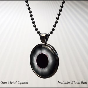 May include: Black gun metal pendant necklace with a black eye design. The pendant has a silver rim and a black ball chain.