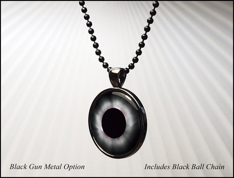 May include: Black gun metal pendant necklace with a black eye design. The pendant has a silver rim and a black ball chain.