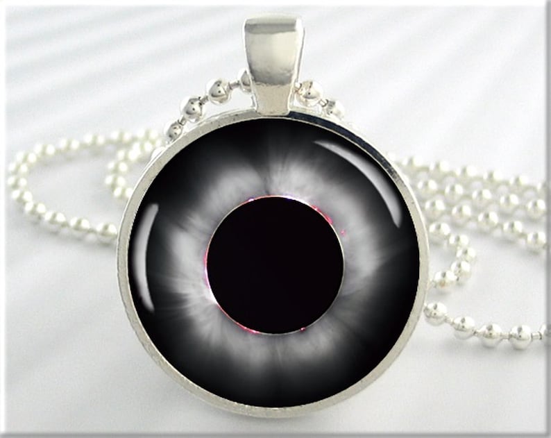May include: A silver necklace with a round pendant featuring a black and white image of an eye with a black pupil and a white iris.