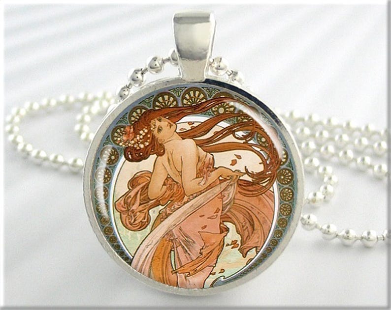 May include: A silver necklace with a round pendant featuring a colorful Art Nouveau illustration of a woman with flowing hair and a floral design. The pendant is surrounded by a decorative border.