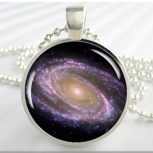 May include: A silver necklace with a round pendant featuring a close-up image of a galaxy with a swirling spiral of pink, purple, and white.