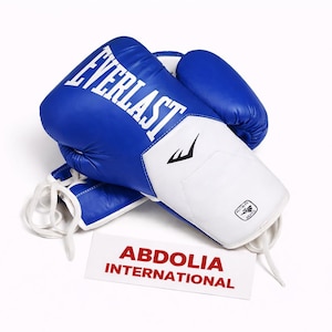 May include: A white ceramic mug with a black handle and the text "But First, Coffee" in a black, handwritten-style font. The mug is on a white surface.