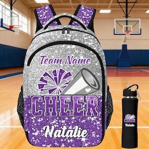 Op de afbeelding: Een zilveren glitterrugzak met een paars en zilverkleurige pompon- en megafoongrafiek, de tekst Team Name, CHEER en Natalie, gecombineerd met een bijpassende zwarte waterfles met dezelfde cheer-afbeelding en de naam Natalie erop gedrukt.