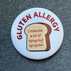 Può includere: Un bottone bianco con le parole "GLUTEN ALLERGY" in rosso sul bordo. Una fetta di pane a cartoni animati è al centro con il testo "I tolerate a lot of things but not gluten".