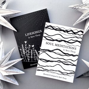 May include: Two black and white illustrated books titled "Lifesongs by Steve Thorp" and "Soul Meditations by Steve Thorp". The books are on a gray surface with white paper stars.