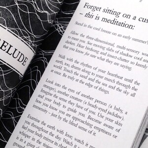 May include: A black and white book with the title "PRELUDE" on the cover. The book is open to a page with the text "Forget sitting on a cushion - this is meditation:" and continues with a paragraph about meditation.