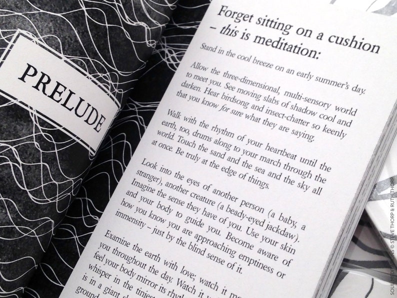 May include: A black and white book with the title "PRELUDE" on the cover. The book is open to a page with the text "Forget sitting on a cushion - this is meditation:" and continues with a paragraph about meditation.