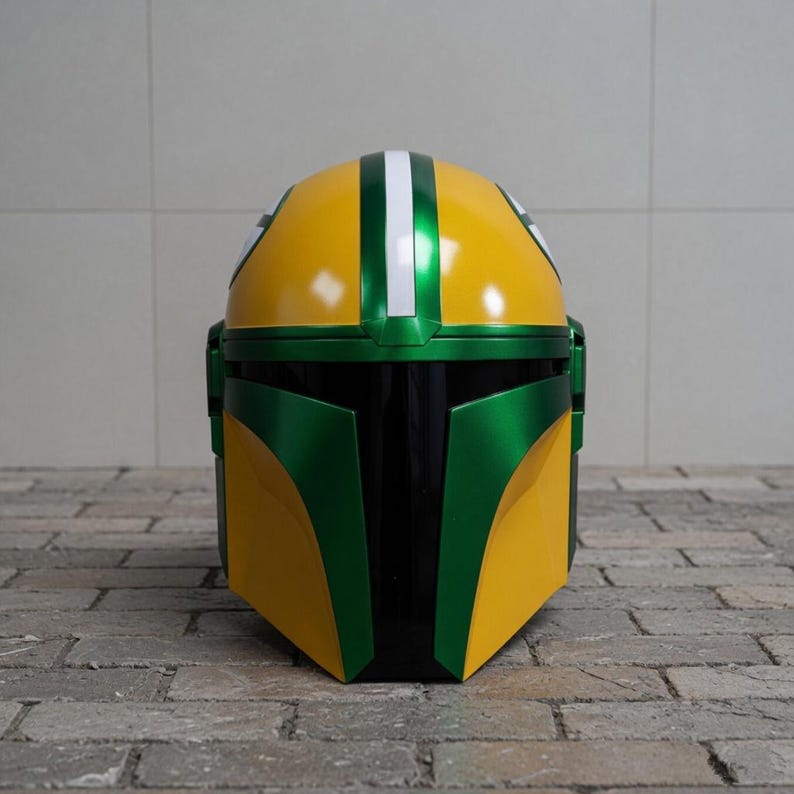 Pu&ograve; includere: Un casco Mandaloriano giallo e verde con finitura lucida. Il casco presenta una parte superiore gialla con una striscia verde e dettagli bianchi, e una piastra frontale verde. Il casco &egrave; progettato con un'estetica elegante e futuristica.
