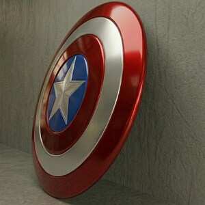 May include: A red, white, and blue shield with a silver star in the center. The shield has a glossy finish and is leaning against a gray wall. The shield is a classic superhero accessory.