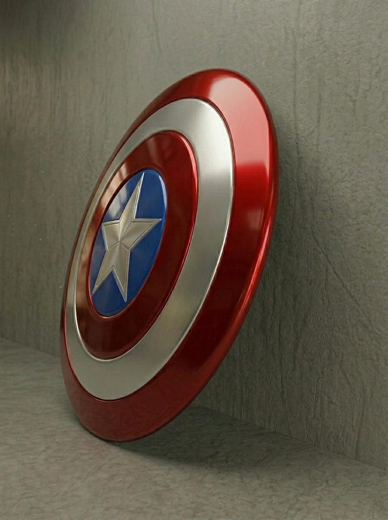 May include: A red, white, and blue shield with a silver star in the center. The shield has a glossy finish and is leaning against a gray wall. The shield is a classic superhero accessory.