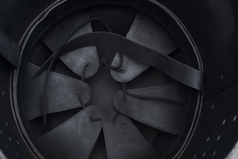 May include: The interior of a black helmet featuring a suspension liner made of six triangular leather flaps. These flaps are connected by thin black cords that lace through eyelets at the top, creating an adjustable fit system inside the shell.