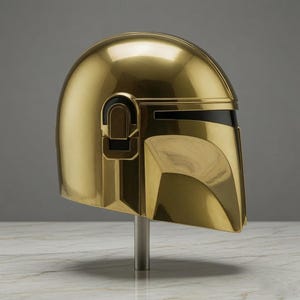 May include: A polished gold-colored helmet featuring a smooth, rounded dome, a T-shaped visor opening with a black horizontal band, and geometric side detailing. The helmet is mounted on a vertical silver-toned metal stand for display purposes.