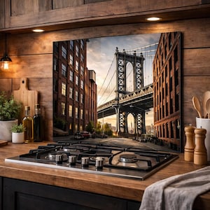 May include: A kitchen backsplash featuring a photograph of the Manhattan Bridge in New York City. The image shows the bridge between two brick buildings, with a view of the city skyline in the background. The backsplash is mounted above a black stovetop.