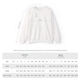 Puede incluir: Una sudadera blanca con cuello redondo y mangas largas. Una tabla de tallas muestra medidas en pulgadas y cent&iacute;metros para ancho, largo y largo de manga, de XS a 5XL.