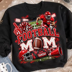 Könnte beinhalten: Ein schwarzes Sweatshirt mit Rundhalsausschnitt und einem Grafikdruck eines Footballspielers in roter Uniform, einem Football, einem roten Helm, einer roten Sporttasche mit der Aufschrift GAMEDAY, einem Megafon, einem Pompon und einem Schaumstofffinger.