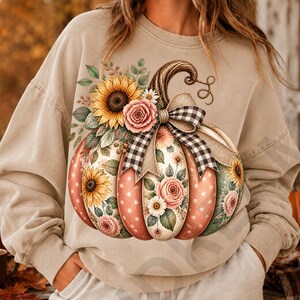 Könnte beinhalten: Ein beigefarbenes Sweatshirt mit Rundhalsausschnitt und einer großen Grafik eines Kürbisses, der mit Sonnenblumen, rosa Rosen und weißen Gänseblümchen verziert ist. Der Kürbis ist mit einer schwarz-weiß karierten Schleife akzentuiert.