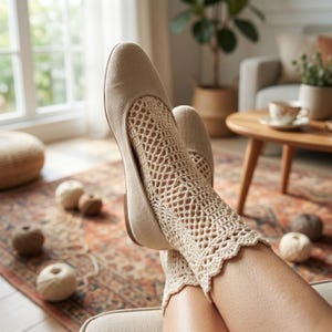 May include: Beige flats with openwork crochet detailing on the top of the foot and ankle. The shoes are worn with matching crochet socks. The image is taken indoors, with a rug and a window in the background.
