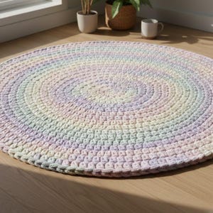 May include: A round, handmade rug with a spiral design. The rug features a gradient of pastel colors, including pink, lavender, yellow, and cream. The rug is made of a thick, textured yarn, and is placed on a wooden floor.