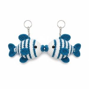 Può includere: Due portachiavi a forma di pesce all'uncinetto, ciascuno con un corpo bianco e strisce, pinne e coda blu. I pesci si baciano, con le labbra che si toccano. Ogni portachiavi ha un anello d'argento attaccato in alto.