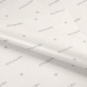 May include: White tissue paper with a repeating pattern of the text "ATELIER WU" and the letter "W" in black. The paper is folded, showing multiple layers and textures.