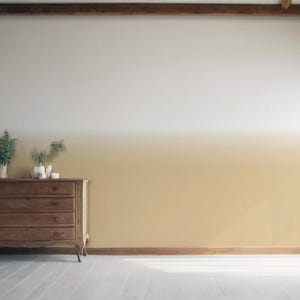 May include: A wooden chest of drawers with four drawers sits against a wall featuring a horizontal ombre paint effect that transitions from a warm golden yellow at the bottom to a crisp white at the top, with green foliage in vases on top.