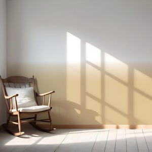 May include: A wooden rocking chair with a white cushion sits in a room with a wall featuring a horizontal ombre paint effect that transitions from white at the top to a warm golden yellow at the bottom, illuminated by natural light from a window.