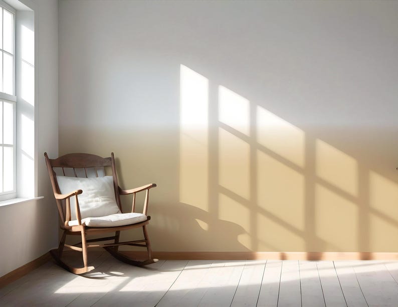 May include: A wooden rocking chair with a white cushion sits in a room with a wall featuring a horizontal ombre paint effect that transitions from white at the top to a warm golden yellow at the bottom, illuminated by natural light from a window.
