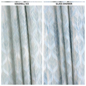 Könnte beinhalten: Zwei hellblaue Gardinenbahnen mit einem sich wiederholenden blattartigen Muster in Weiß. Auf der linken Seite steht "SEASHELL ICE" und auf der rechten Seite "GLASS SHOWER". Der Stoff hat einen dezenten Glanz und eine strukturierte Optik.