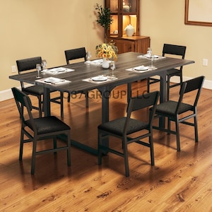 May include: A dark gray rectangular dining table with eight matching black chairs. The table is set with white plates, silverware, and glasses. The chairs have black fabric seats and backs. The table is in a room with hardwood floors.